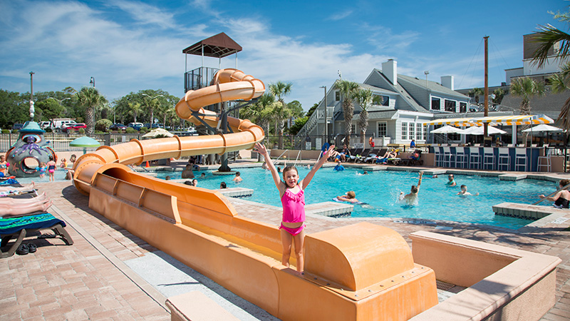Girl in pink bathing suit standing a bottom of waterslide with arms raised