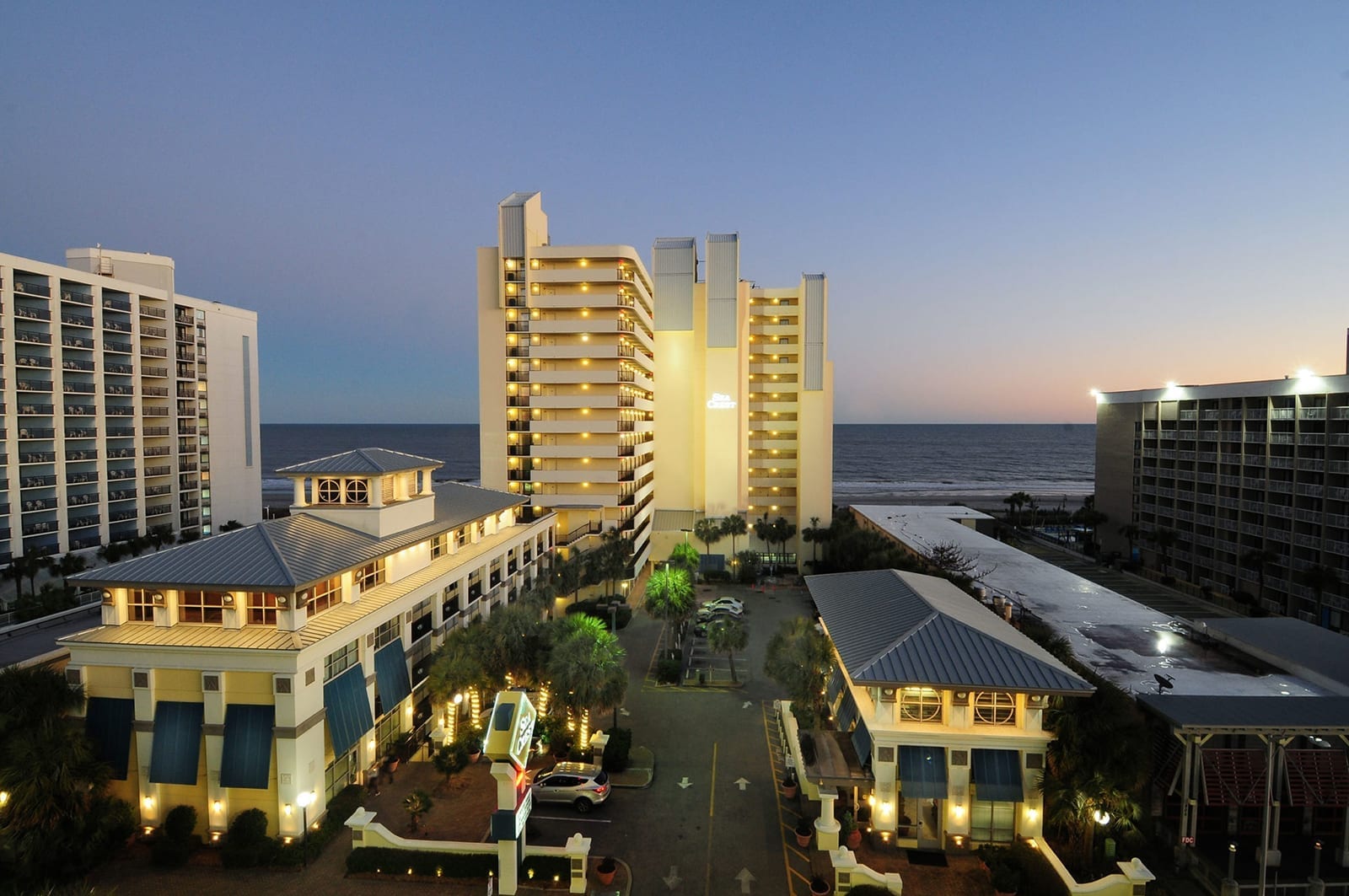 Oceanfront resort at twilight with illuminated high-rise towers, beachfront hotels, and sandy shores perfect for coastal getaways.