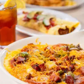 Loaded breakfast omelette with melted cheese, ham, and peppers served with fresh juice and pastries for a delightful dining experience.