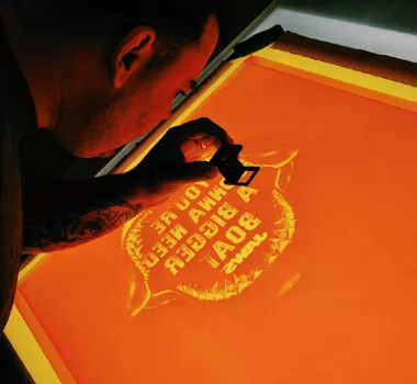 Close up shot of a worker screen printing a logo on an orange screen.