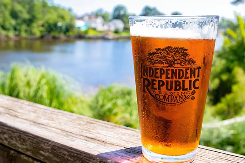 Glass of beer with Independent Republic logo on outdoor railing overlooking water 