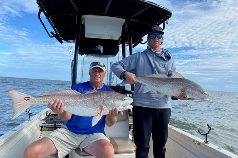 Two men on fishing boat each holding a big fish