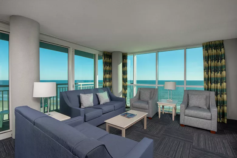 Living room with two sofas, two chairs, and floor to ceiling windows with oceanfront views