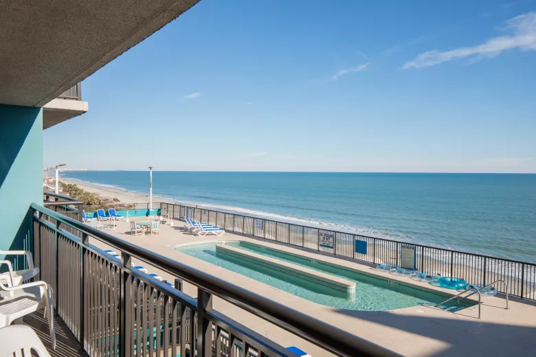 A balcony overlooking a rooftop pool with lazy river and oceanfront views