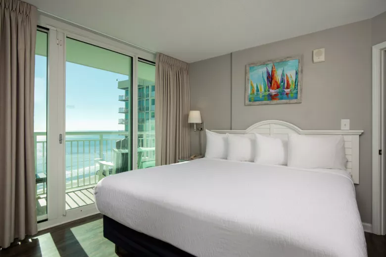 Oceanfront king bedroom with white linens and large window with ocean view