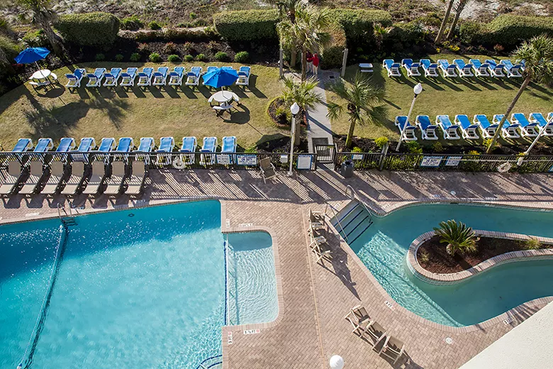 Overview of an outdoor pool deck with swimming pools, lazy rivers, and a green grassy lawn area with lounge chairs