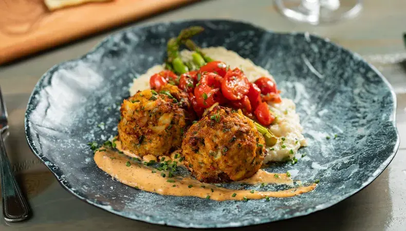 Gourmet plated dish featuring golden meatballs with fresh tomato relish and creamy sauce on modern dinnerware.