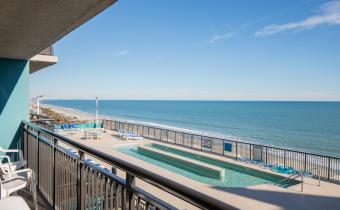 A balcony overlooking a rooftop pool with lazy river and oceanfront views