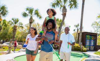 Family playing mini golf - son on dad's shoulders