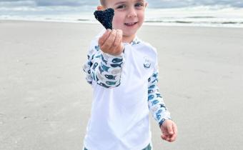 a child poses on the beach with a found shark tooth