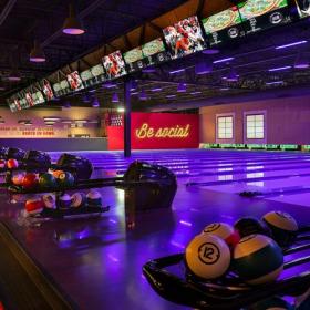 Darkly lit empty bowling lanes with Be Social sign in background