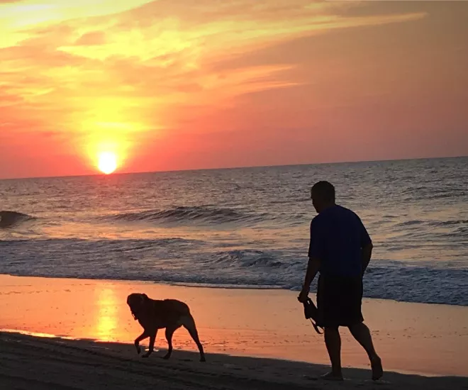 Man and dog walking on the beach at sunset