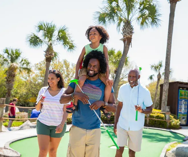 Family playing mini golf - son on dad's shoulders