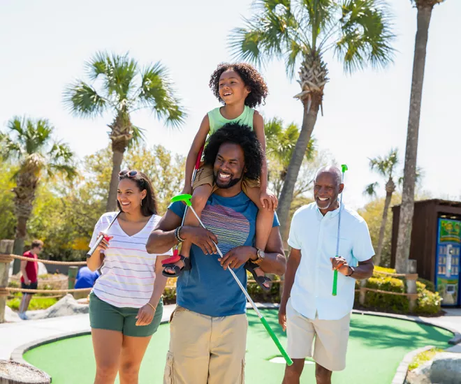 Family playing mini golf - son on dad's shoulders