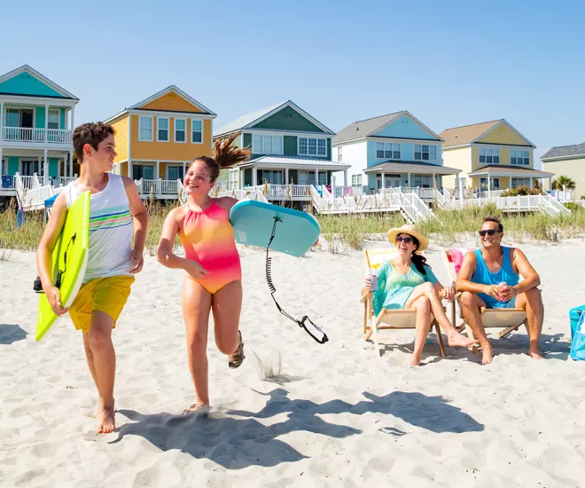 Family on beach with beach home kids running with boogie boards