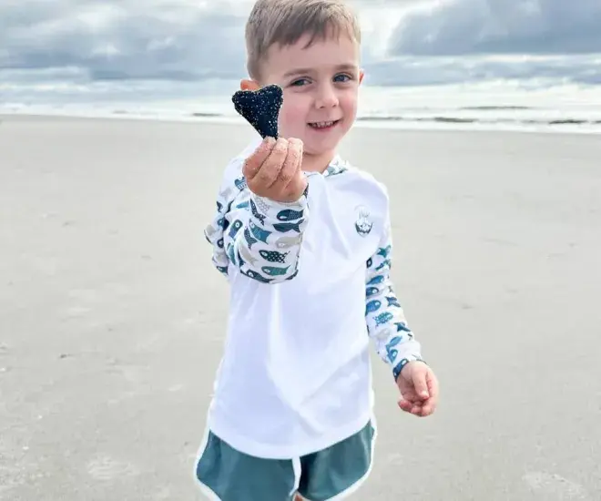 a child poses on the beach with a found shark tooth