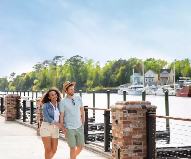 A couple walking alongside a river bank. 