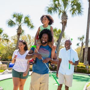Family playing mini golf - son on dad's shoulders