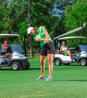 Female golf with golf carts behind her
