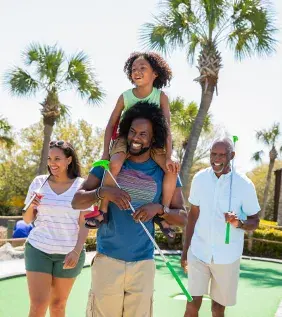 Family playing mini golf - son on dad's shoulders