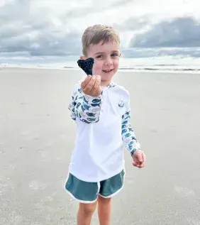 a child poses on the beach with a found shark tooth