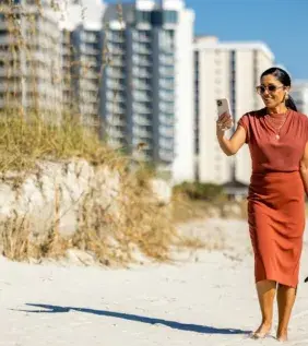 Woman in business attired walking barefoot on the beach holding shoes