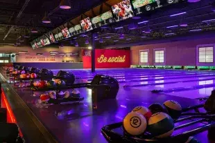 Darkly lit empty bowling lanes with Be Social sign in background