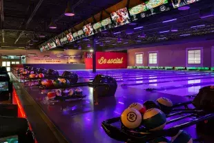 Darkly lit empty bowling lanes with Be Social sign in background