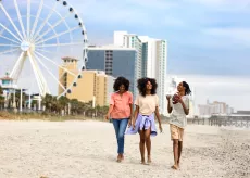 Teens walking with mom on the beach near skywheel