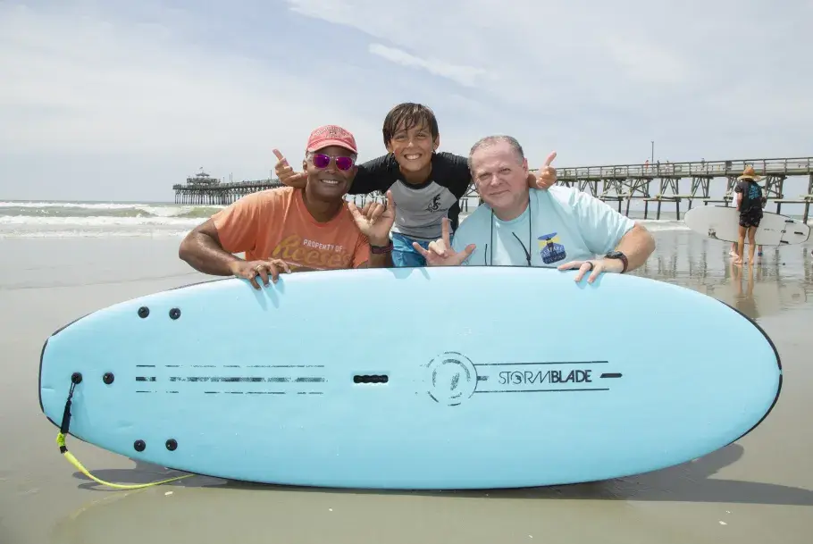 3 participants pose with a board at Cherry Grove Pier Surf Camp