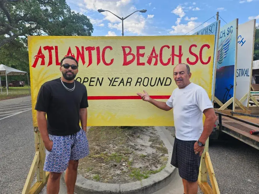 Atlantic Beach mural that features "Open Year Round" with two gentlemen posing in front of it.