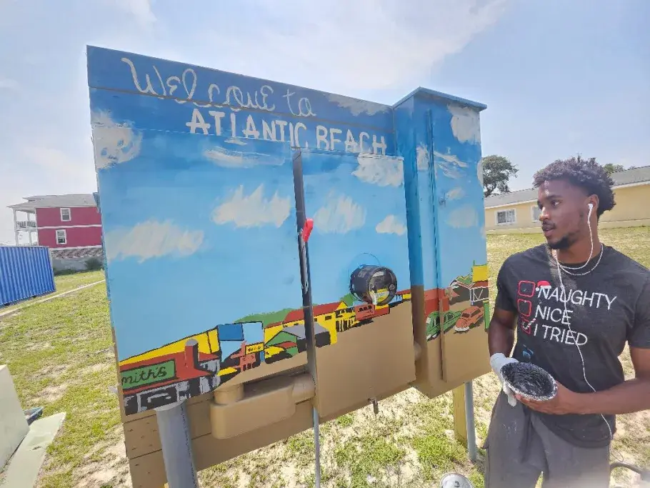 Christopher Carlisle posing with a Welcome to Atlantic Beach mural he painted.